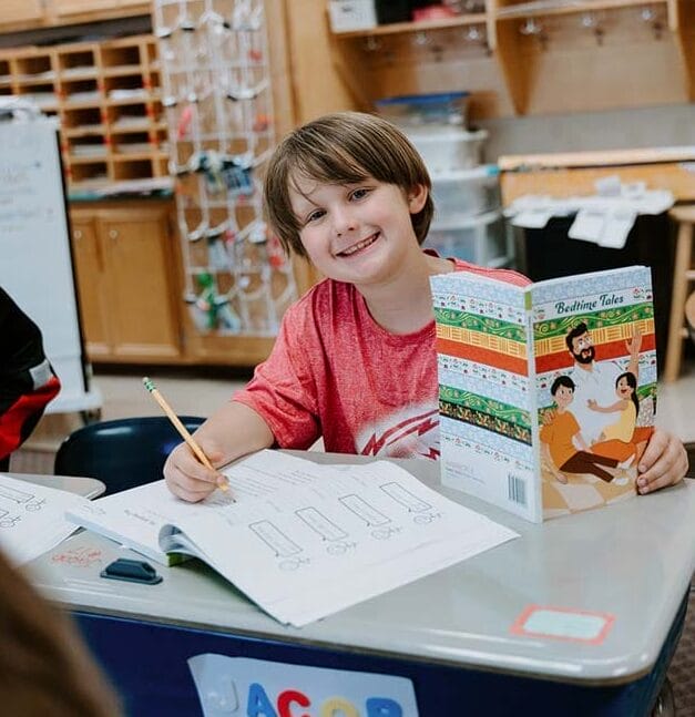 Students in classroom, sitting at tables, reading and coloring.