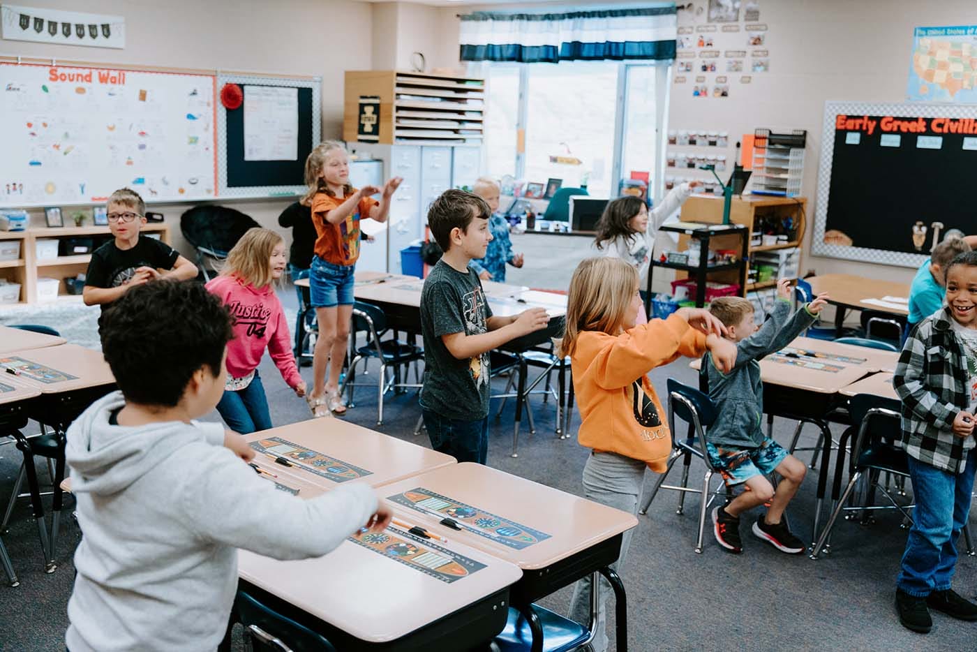 Students in classroom, sitting either on the floor or in a chair, participating in classroom activities