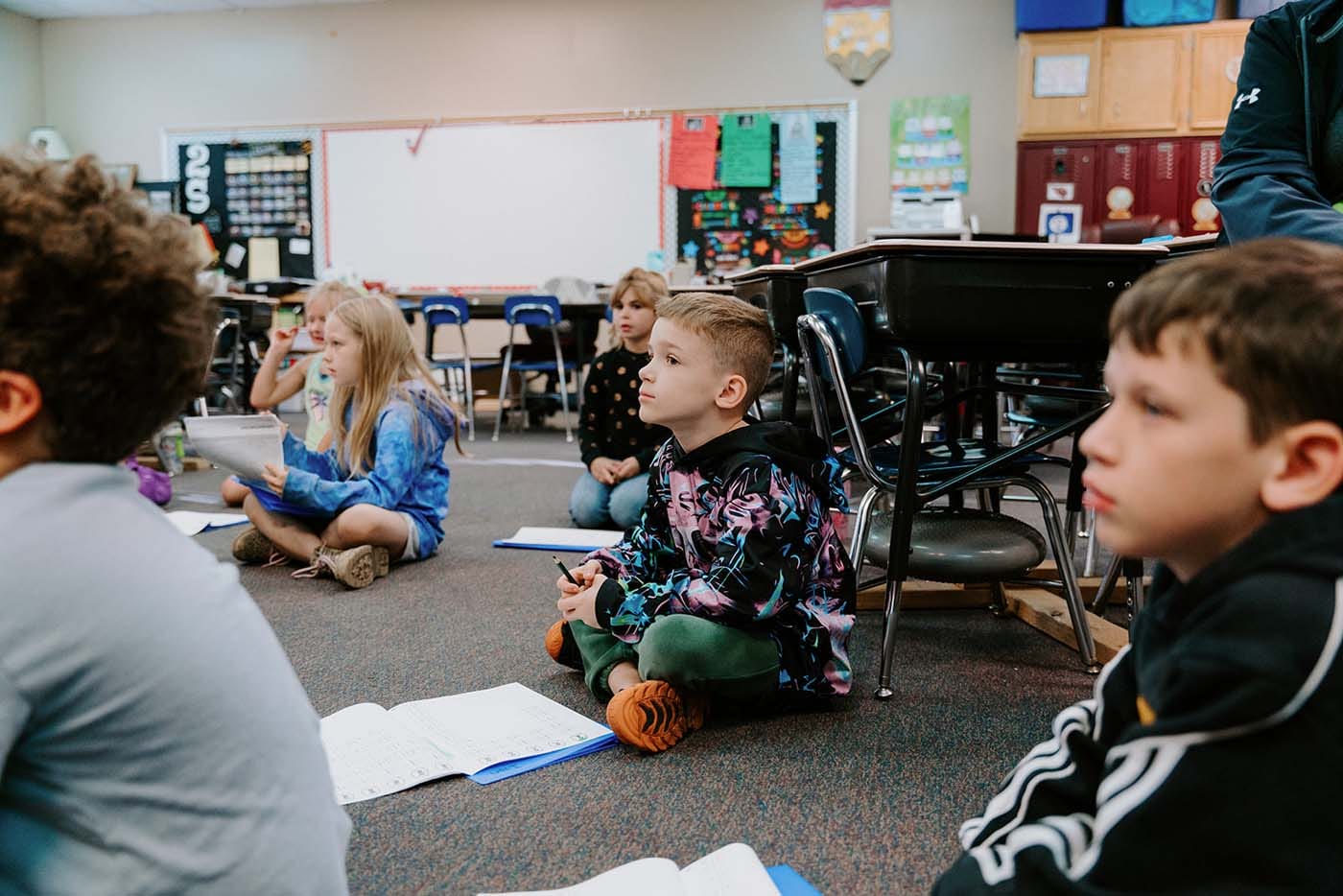 Students in classroom, sitting either on the floor or in a chair, participating in classroom activities