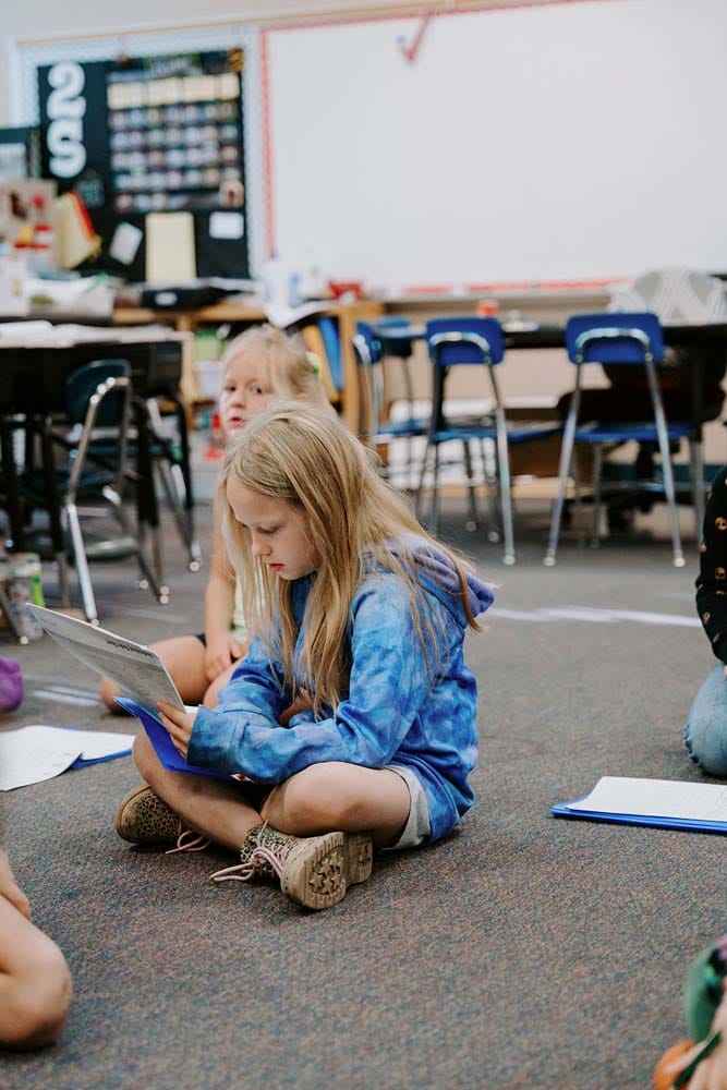 Students in classroom, sitting either on the floor or in a chair, participating in classroom activities