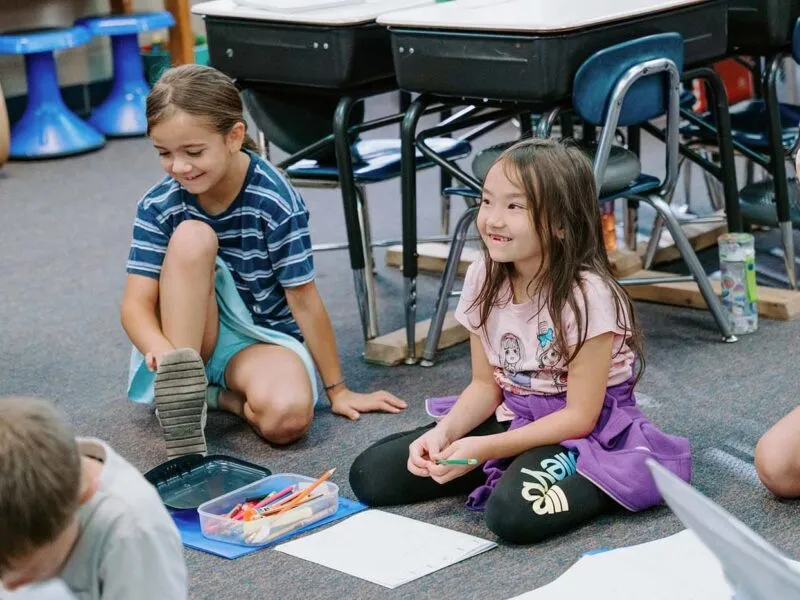 Students in classroom, sitting either on the floor or in a chair, participating in classroom activities