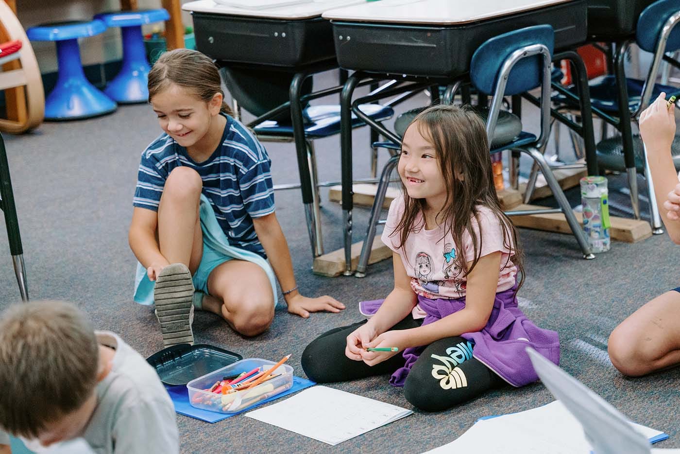 Students in classroom, sitting either on the floor or in a chair, participating in classroom activities
