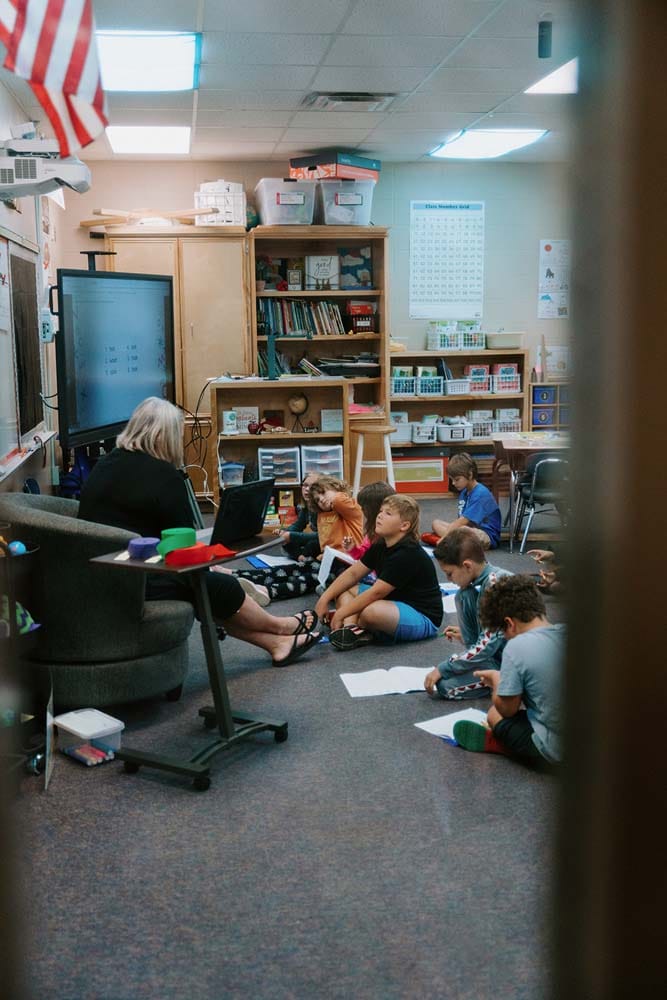 Students in classroom, sitting either on the floor or in a chair, participating in classroom activities