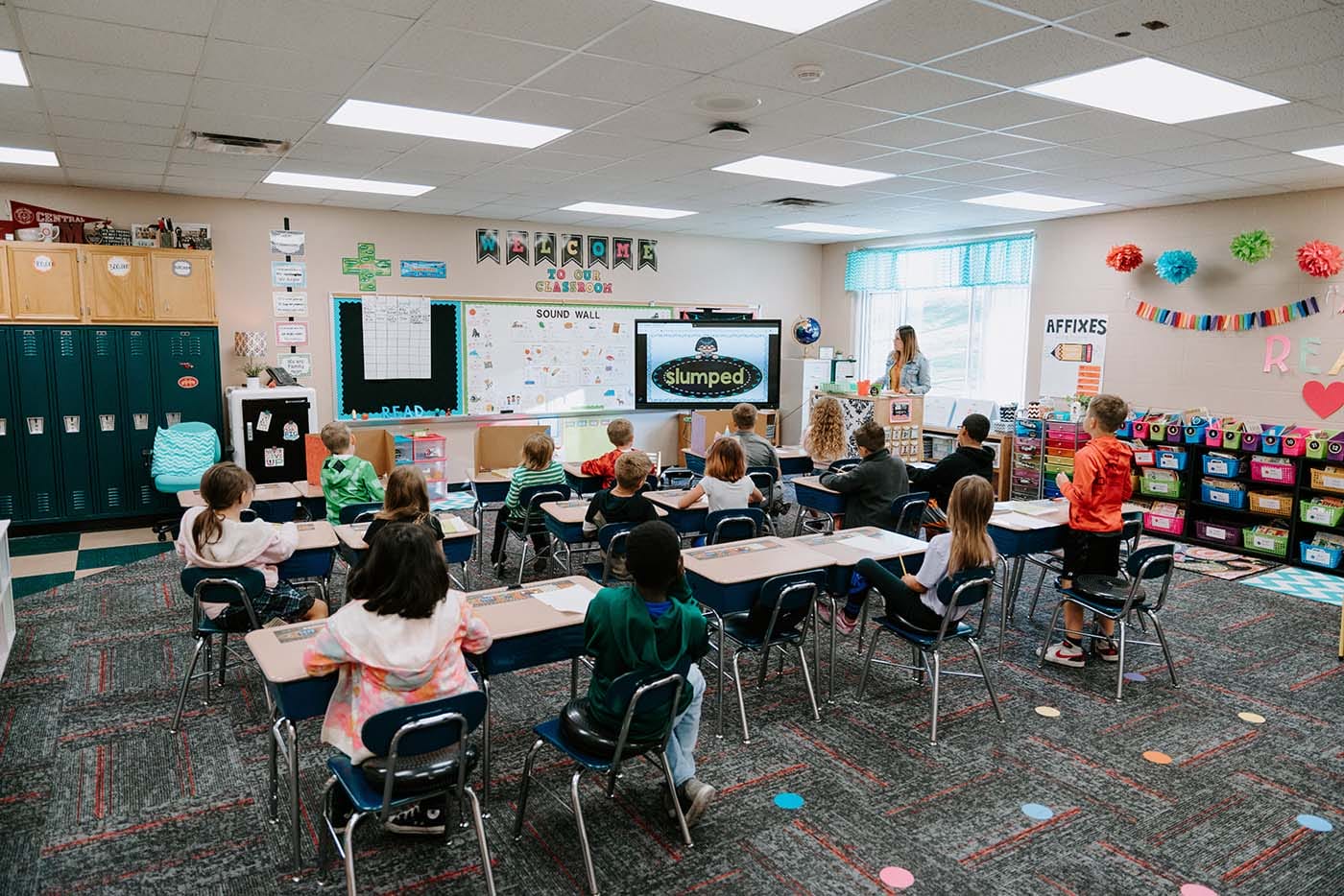 Students in classroom, sitting either on the floor or in a chair, participating in classroom activities