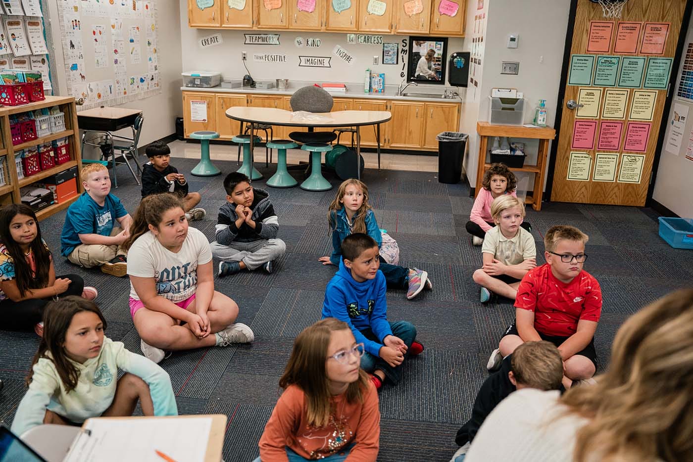 Students in a classroom engaging in classroom activities while sitting on the floor.