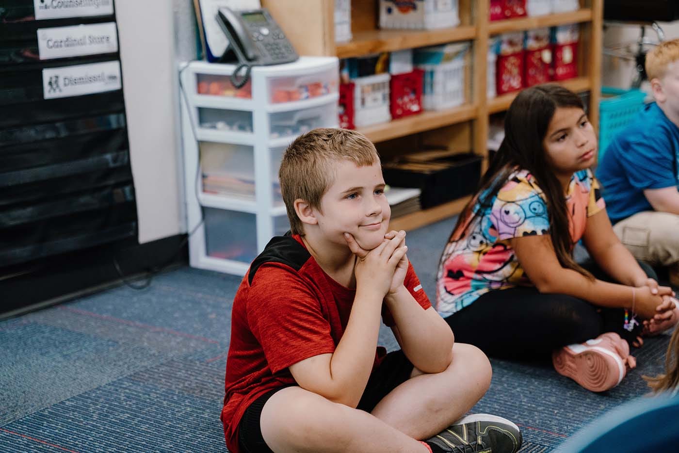 Students in a classroom engaging in classroom activities while sitting on the floor.