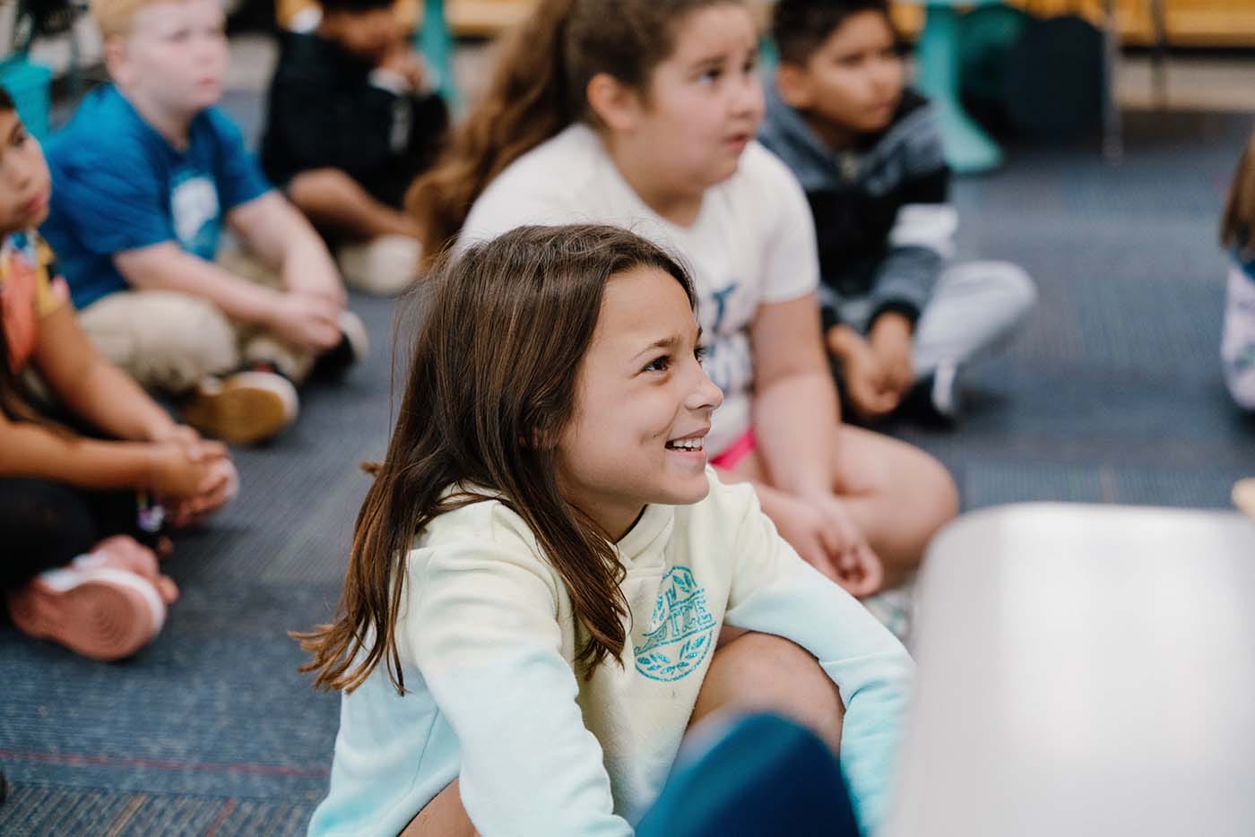 Students in a classroom engaging in classroom activities while sitting on the floor.