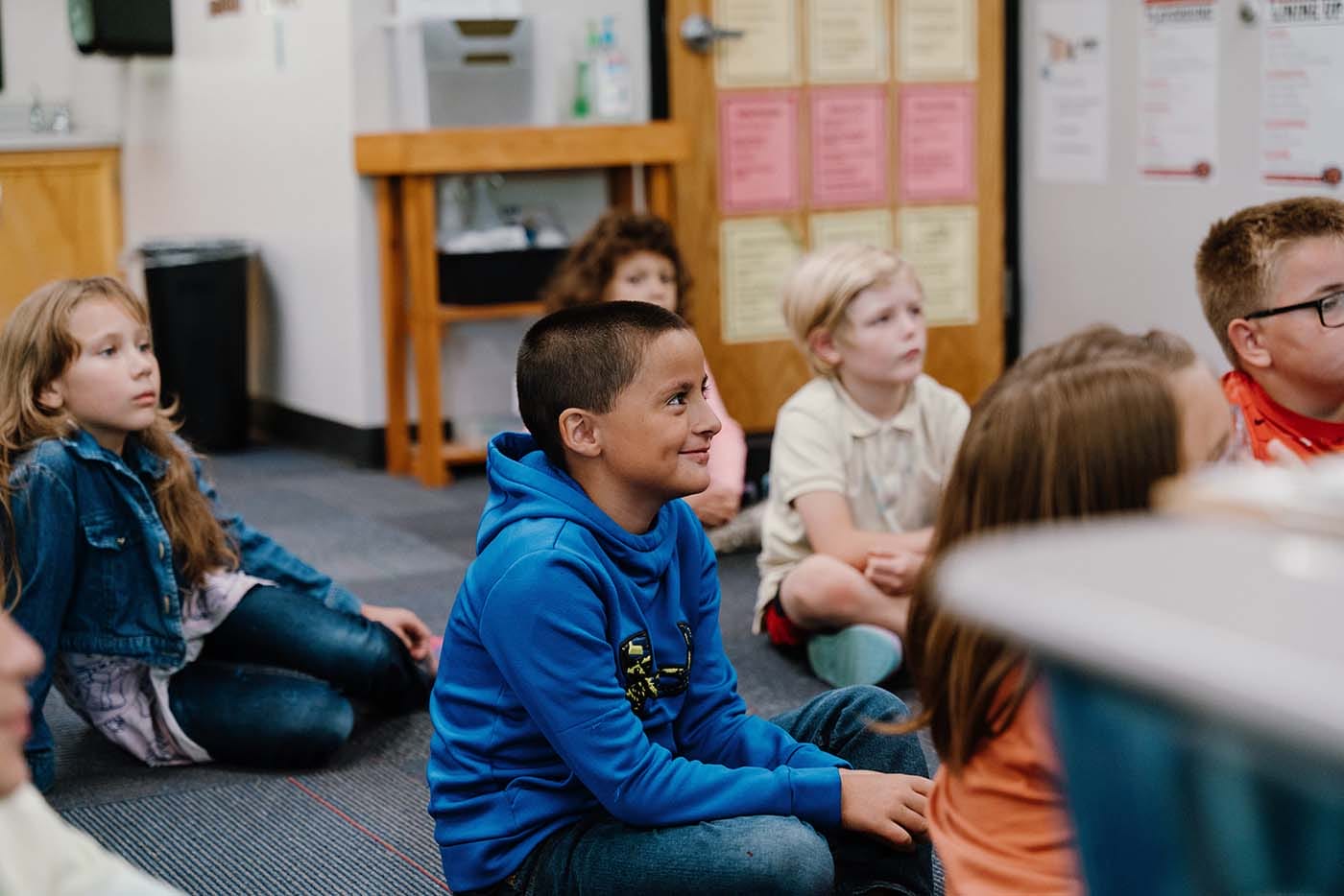 Students in a classroom engaging in classroom activities while sitting on the floor.