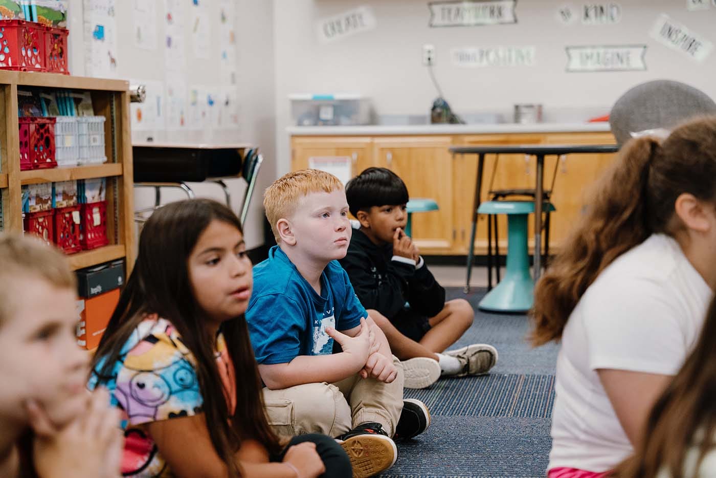 Students in a classroom engaging in classroom activities while sitting on the floor.