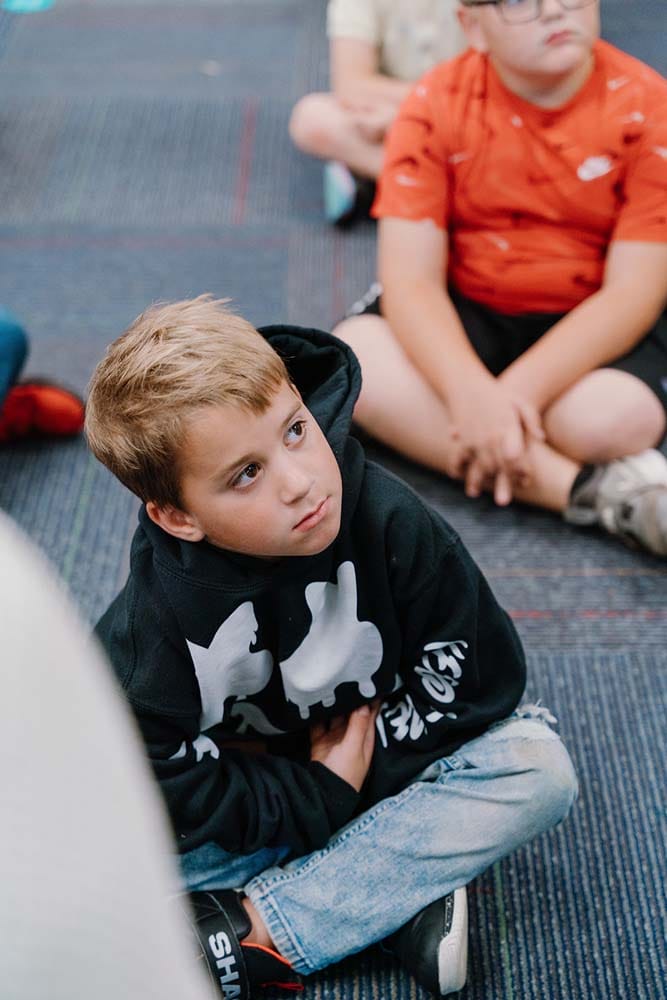 Students in a classroom engaging in classroom activities while sitting on the floor.