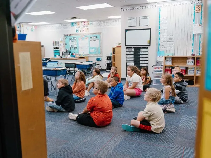 Students in a classroom engaging in classroom activities while sitting on the floor.