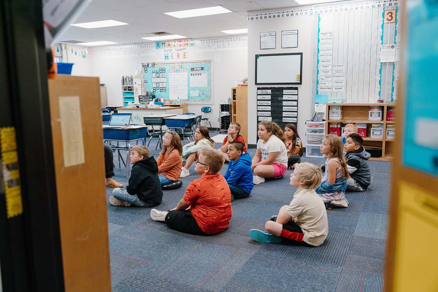 Students in a classroom engaging in classroom activities while sitting on the floor.