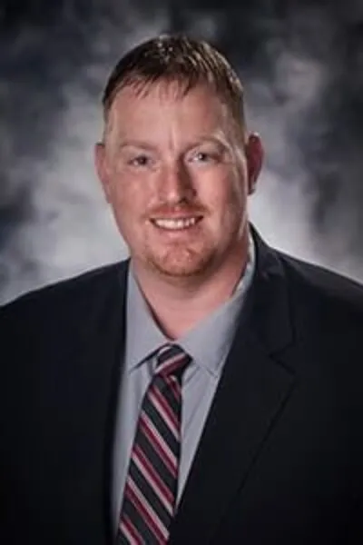 Portrait of a man in a dark suit and striped tie, smiling in front of a smoky gray studio backdrop.